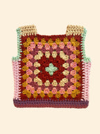 A handmade crocheted granny square vest with shoulder straps, featuring a multicolor pattern of pink, yellow, brown, and purple squares 