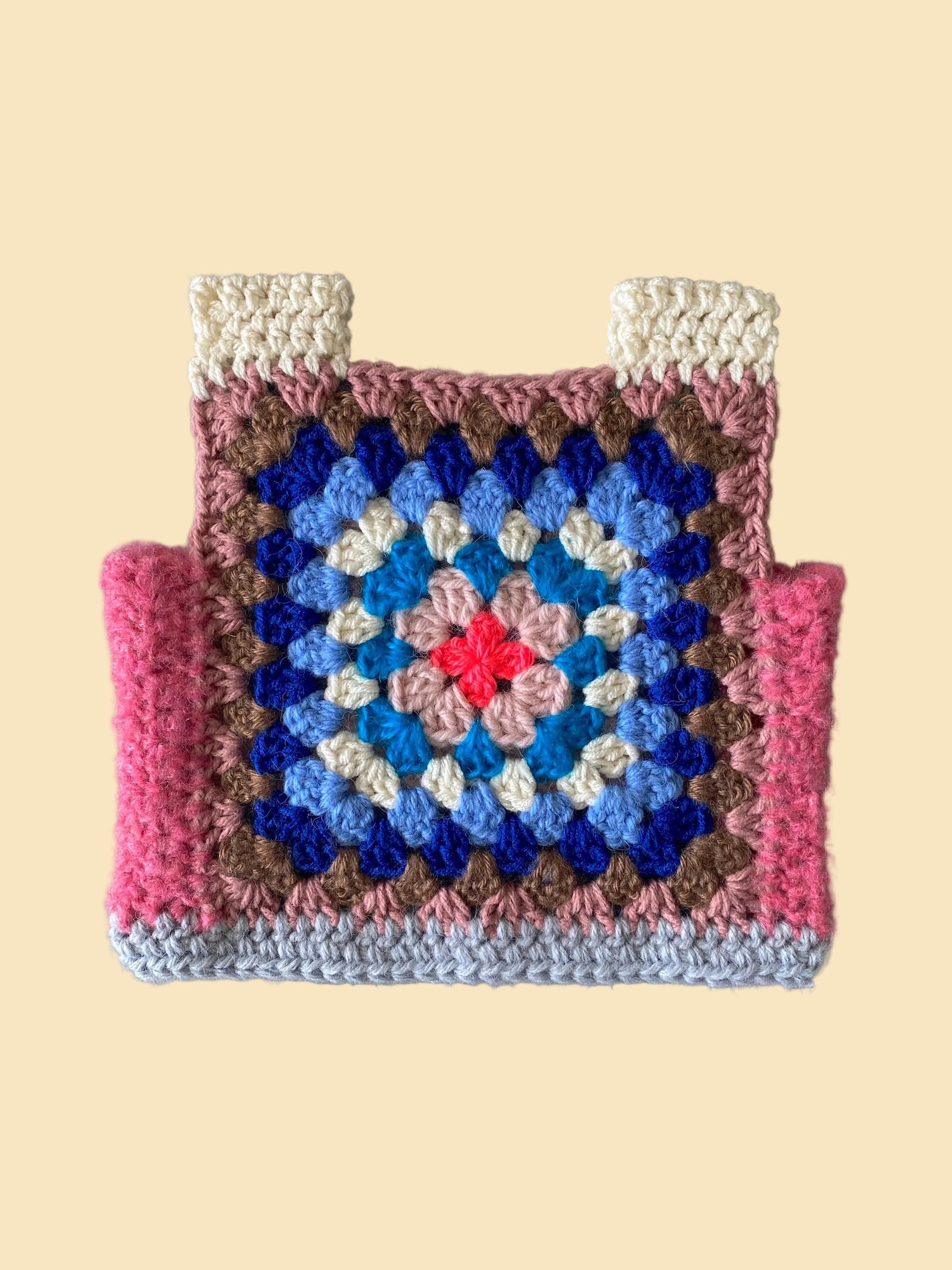 Crocheted kid vest with a colorful square pattern on a plain background