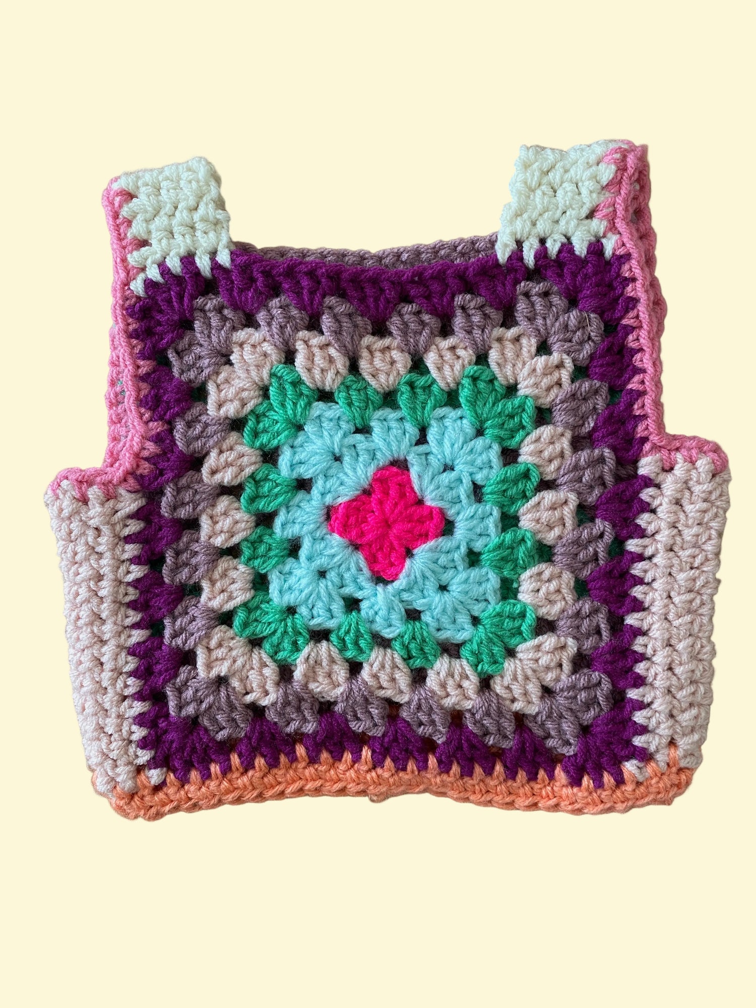 Colorful crocheted vest with a pink center on a wooden surface