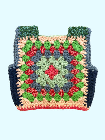 A handmade crocheted granny square vest with a colorful geometric pattern, featuring green, blue, red, pink, and beige yarn, laid flat on a light beige textured background.