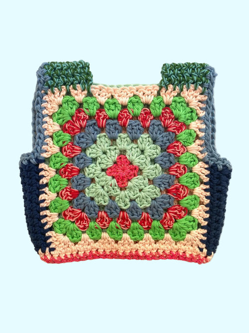 A handmade crocheted granny square vest with a colorful geometric pattern, featuring green, blue, red, pink, and beige yarn, laid flat on a light beige textured background.