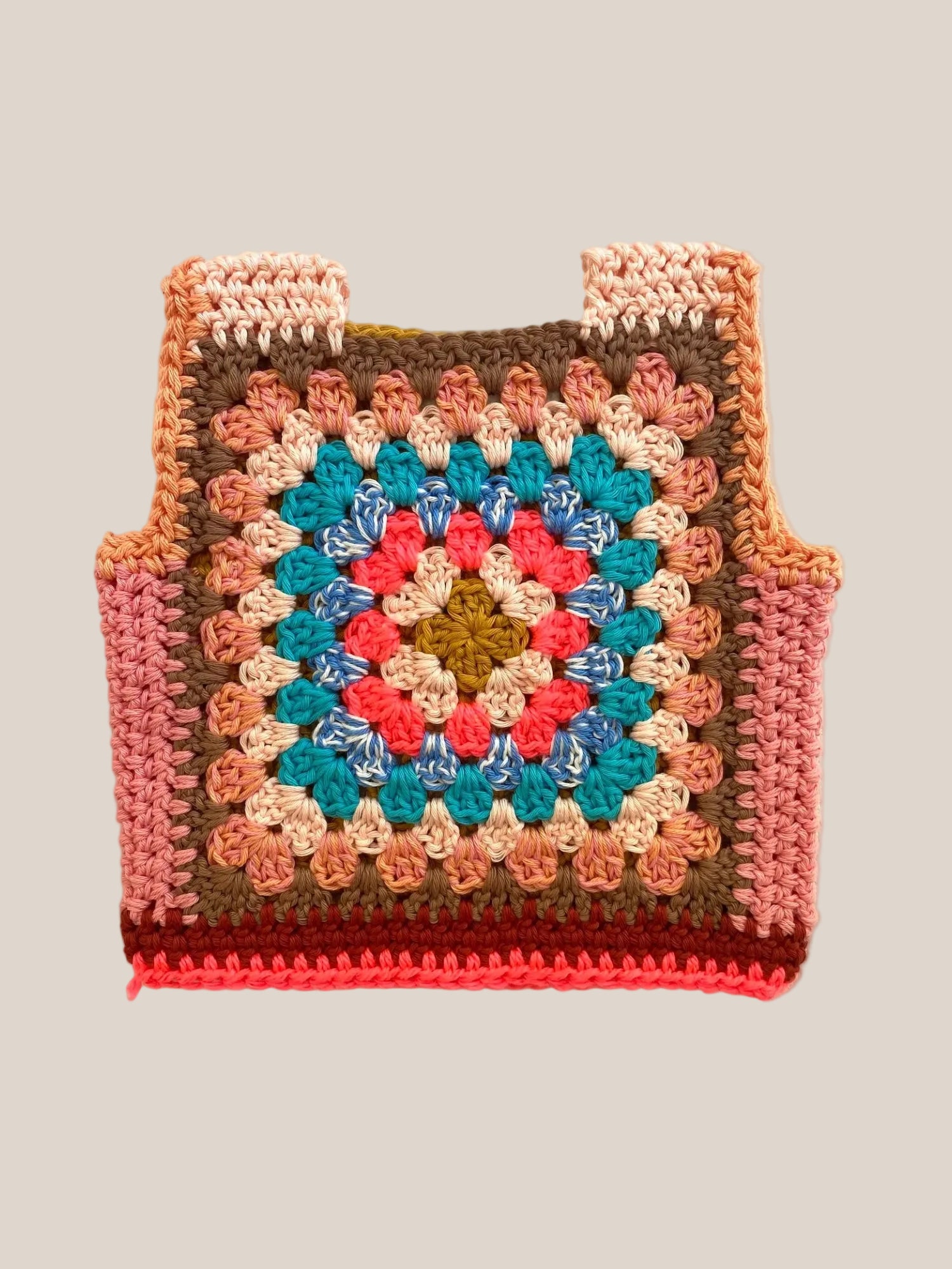 A handmade crocheted granny square ves with a colorful geometric pattern, laid flat on a light beige fabric background.