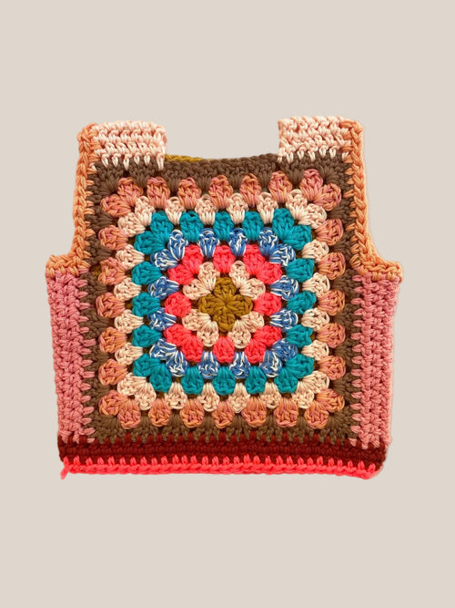 A handmade crocheted granny square ves with a colorful geometric pattern, laid flat on a light beige fabric background.
