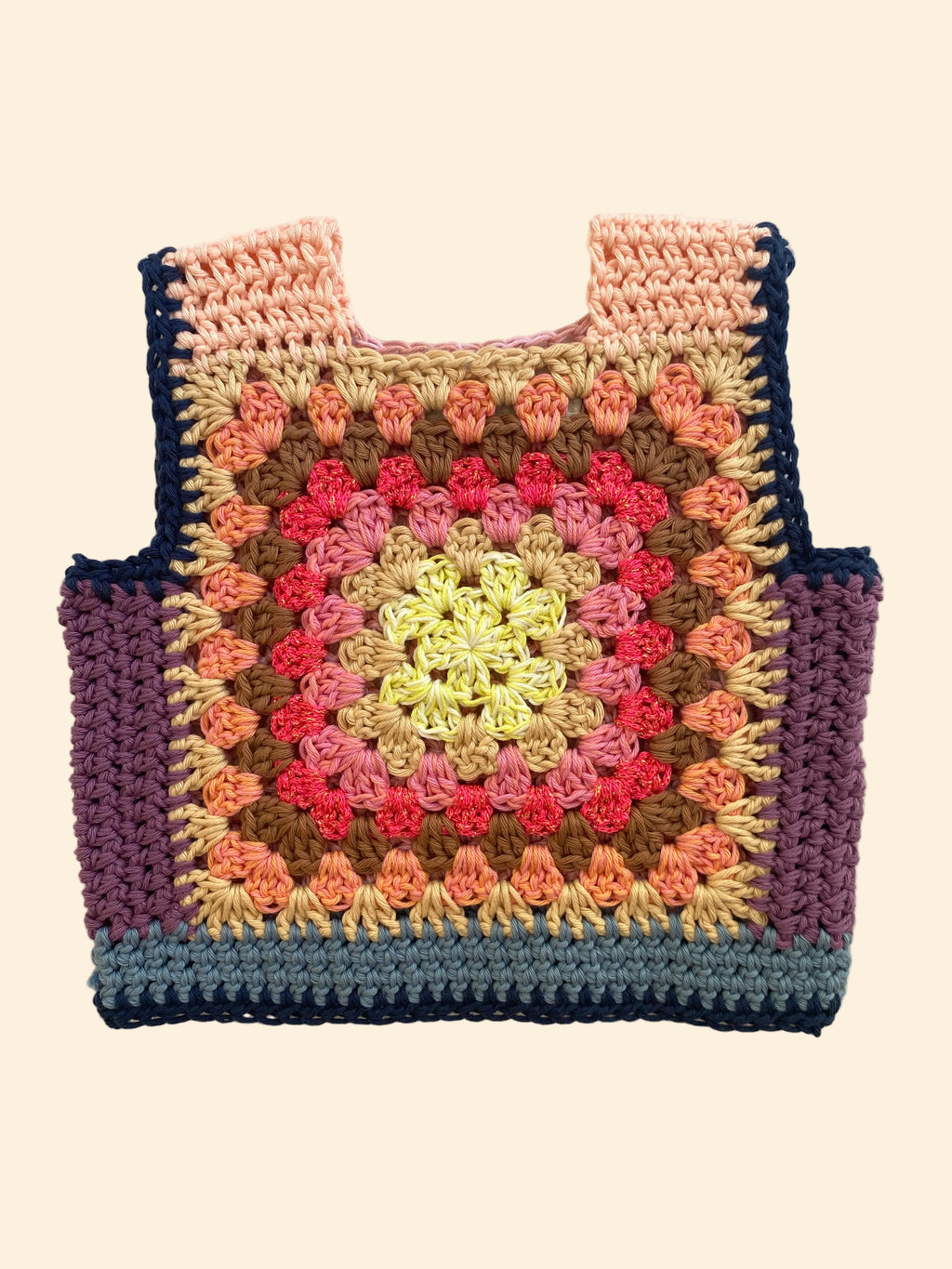 A handmade crocheted tote vest with a colorful granny square pattern, laid flat on a light beige fabric background.