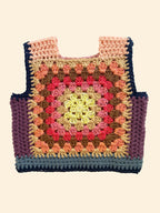 A handmade crocheted tote vest with a colorful granny square pattern, laid flat on a light beige fabric background.