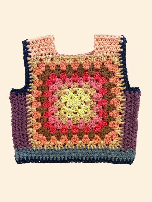 A handmade crocheted tote vest with a colorful granny square pattern, laid flat on a light beige fabric background.