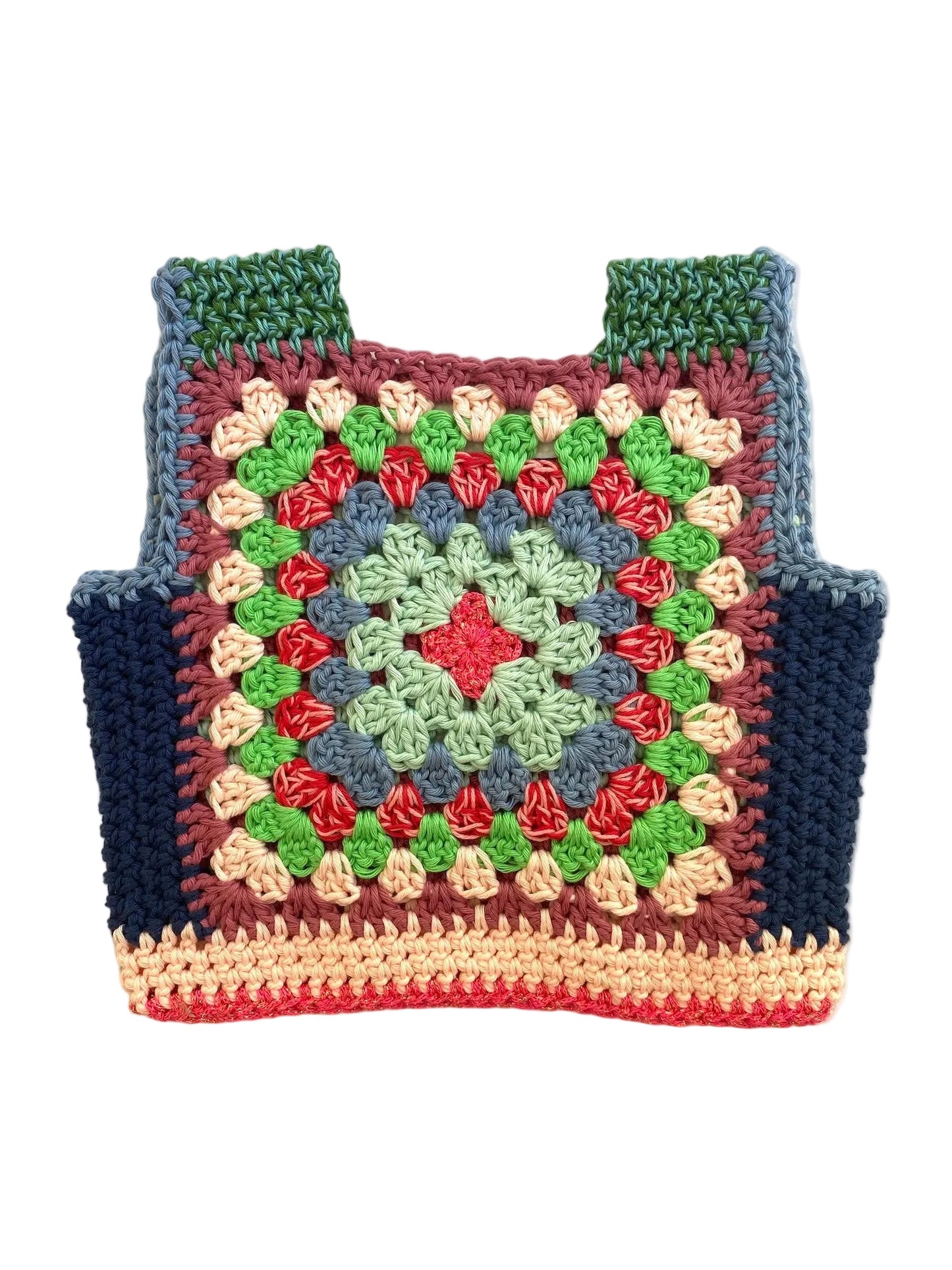 A handmade crocheted granny square vest laid flat on a light beige fabric background. The bag features a multicolor pattern with green, blue, red, pink, and cream yarn, and has shoulder straps at the top.
