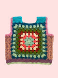 A handmade crocheted tote vest featuring a colorful granny square pattern with teal, pink, green, red, and cream yarn, laid flat on a light beige fabric background.