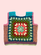 A handmade crocheted tote vest featuring a colorful granny square pattern with teal, pink, green, red, and cream yarn, laid flat on a light beige fabric background.