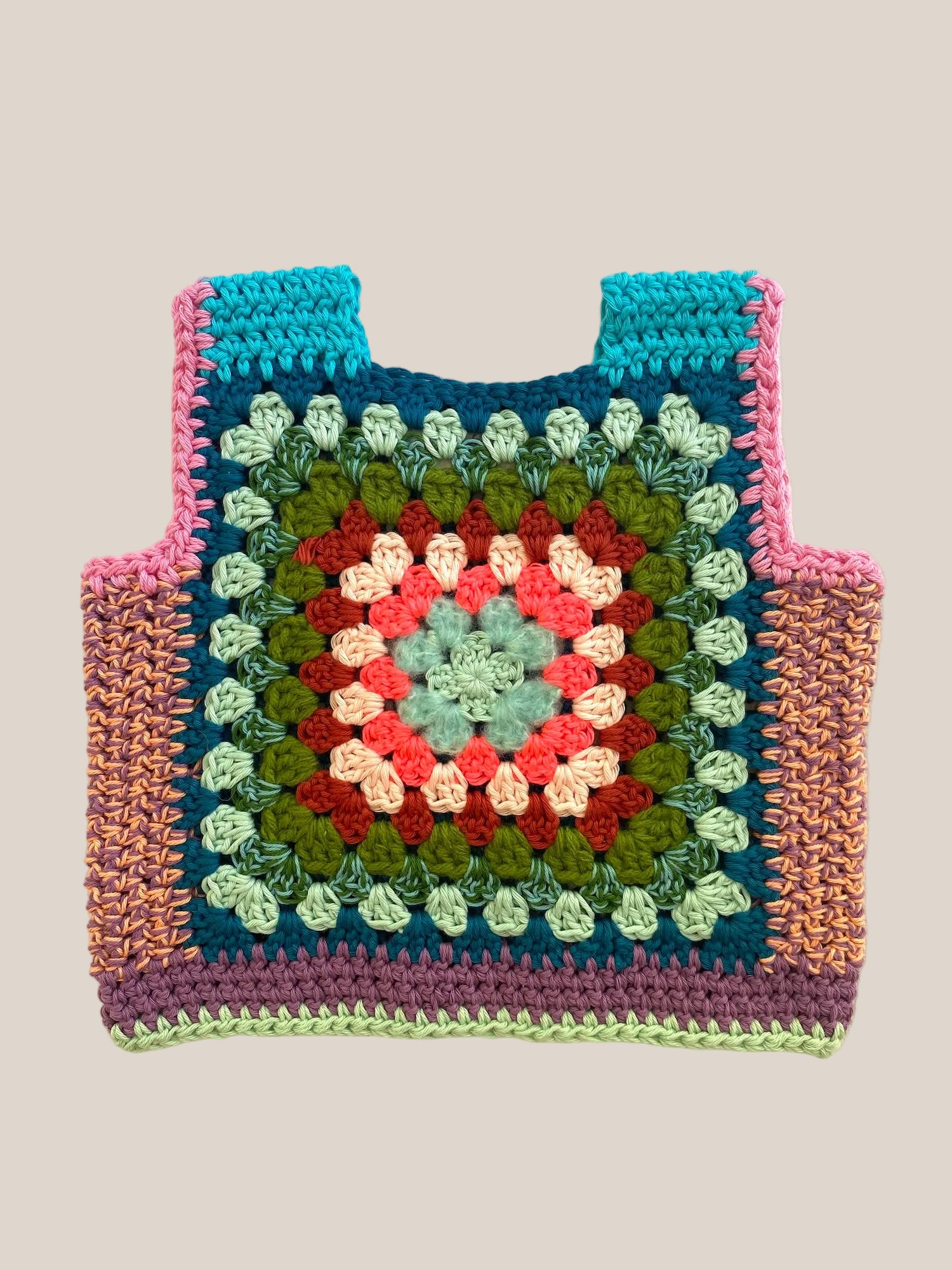 A handmade crocheted tote vest featuring a colorful granny square pattern with teal, pink, green, red, and cream yarn, laid flat on a light beige fabric background.