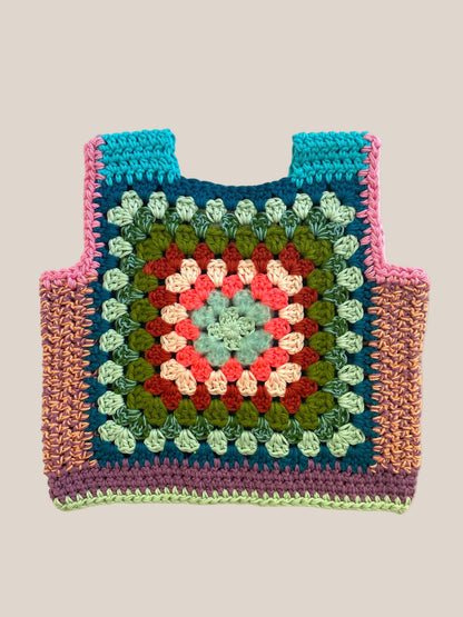 A handmade crocheted tote vest featuring a colorful granny square pattern with teal, pink, green, red, and cream yarn, laid flat on a light beige fabric background.